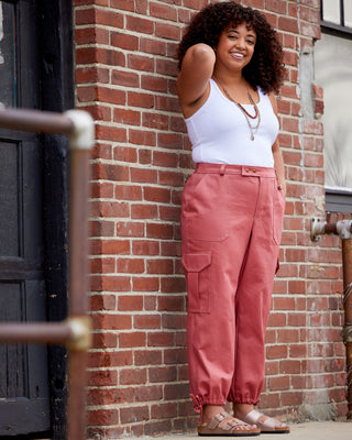 Woman wearing a white tank top and pink pants leaning against a brick wall. These pants are the Esmond Cargo Pants sewing pattern from Cashmerette.