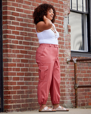 Woman wearing a white top and pink pants leaning against a brick wall. These pants are the Esmond Cargo Pants sewing pattern from Cashmerette.
