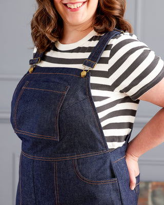 Person wearing a striped shirt and denim overalls against a neutral background. These overalls are the Rhinecliff Overalls sewing pattern from Cashmerette.