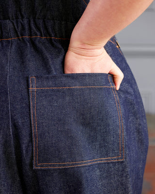 Person wearing a dark blue denim apron with a pocket. These overalls are the Rhinecliff Overalls sewing pattern from Cashmerette.