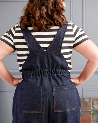 Person wearing a striped shirt and denim overalls with a neutral background These overalls are the Rhinecliff Overalls sewing pattern from Cashmerette.