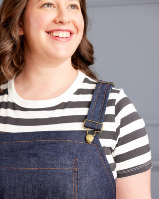 Person wearing a striped shirt and denim overalls against a neutral background. These overalls are the Rhinecliff Overalls sewing pattern from Cashmerette.