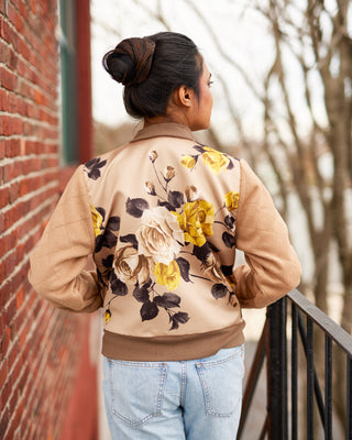 Person wearing a beige bomber jacket with floral patterns standing against a brick wall. This jacket is the Cashmerette Club Kimball Bomber Jacket sewing pattern.