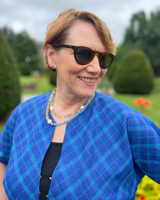 Woman wearing a blue checkered jacket and sunglasses outdoors with greenery in the background.  This jacket is the Catskills Bias Jacket sewing pattern from Cashmerette.