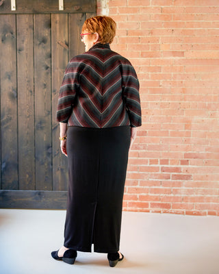 Person wearing a patterned jacket and black pants standing against a brick wall. This jacket is the Catskills Bias Jacket sewing pattern from Cashmerette.