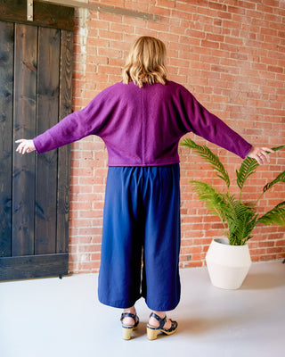 Person wearing a purple sweater and blue pants standing in front of a brick wall. This jacket is the Catskills Bias Jacket sewing pattern from Cashmerette.
