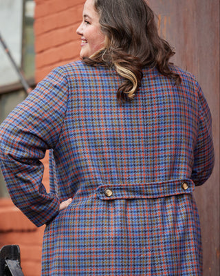 Woman wearing a plaid coat standing against a textured wall. This coat is the Newcomb Car Coat sewing pattern from Cashmerette.