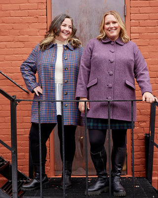 Two women wearing colorful coats standing on a metal staircase against a brick wall. This coat is the Newcomb Car Coat sewing pattern from Cashmerette.