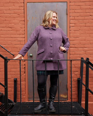 Woman in a purple coat standing on a staircase against a red brick wall. This coat is the Newcomb Car Coat sewing pattern from Cashmerette.