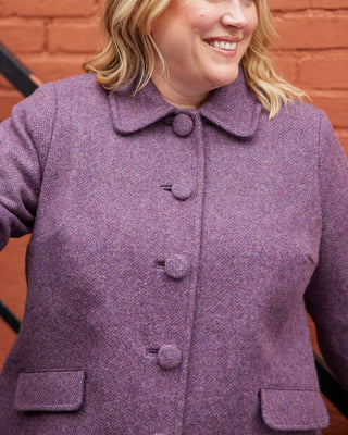 Purple coat worn by a person with a brick wall background. This coat is the Newcomb Car Coat sewing pattern from Cashmerette.
