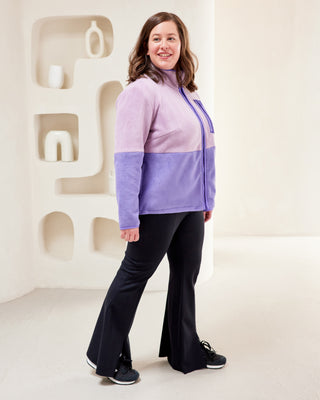 Woman wearing a two-tone purple sweater and black pants standing in a minimalistic room. This jacket is the Hatton Fleece Jacket sewing pattern from Cashmerette.