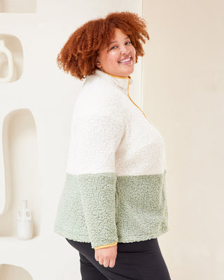 Person wearing a two-tone jacket with white top and green bottom in a minimalistic setting. This jacket is the Hatton Fleece Jacket sewing pattern from Cashmerette.