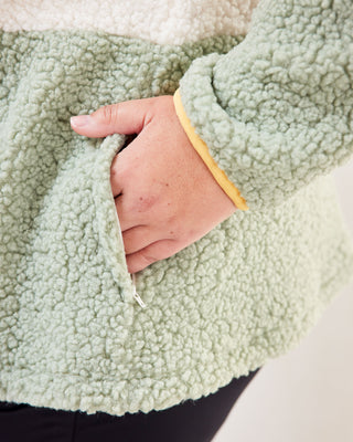 Close-up of a hand holding green fleece fabric with a blurred background. This jacket is the Hatton Fleece Jacket sewing pattern from Cashmerette.