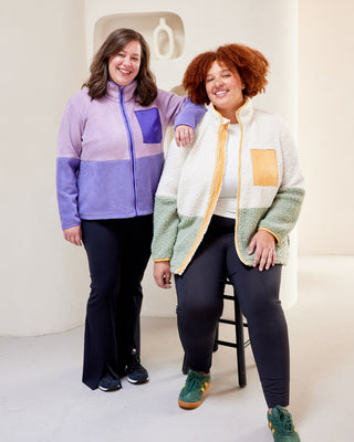 Two women wearing colorful jackets standing in a studio setting. This jacket is the Hatton Fleece Jacket sewing pattern from Cashmerette.