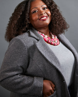 Woman wearing a gray coat and pink necklace against a gray background. This blazer is the Auburn Blazer sewing pattern from Cashmerette.