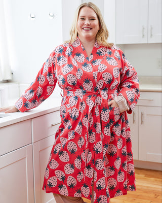 Woman wearing a red strawberry patterned robe in a kitchen.  This robe is the Lygon Robe sewing pattern from Cashmerette.