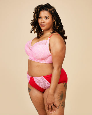Woman wearing a pink lace bralette and red high-waisted underwear on a beige background. This bra is the Willowdale Bra sewing pattern from Cashmerette.