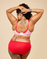 Person wearing a pink bikini top and red bottoms against a beige background. This bra is the Willowdale Bra sewing pattern from Cashmerette.