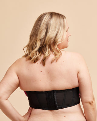Woman wearing a black strapless top against a beige background. This bra is the Symmes Strapless Bra sewing pattern from Cashmerette.