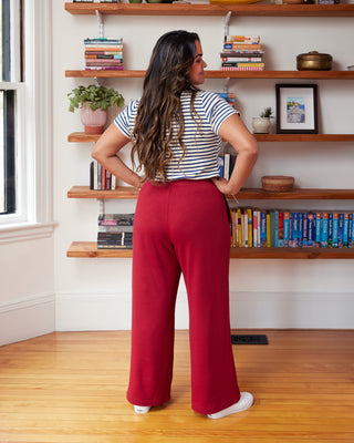 Woman in red pants and striped shirt standing in a room with wooden shelves and books. These pants are the Ardley Elastic Waist Pants sewing pattern from "Sewing the Curve" by Jenny Rushmore.