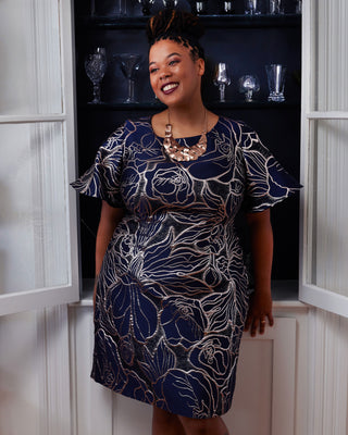 Woman wearing a blue patterned dress standing in a doorway. This dress is the Elmley Sheath Dress sewing pattern from "Sewing the Curve" by Jenny Rushmore.