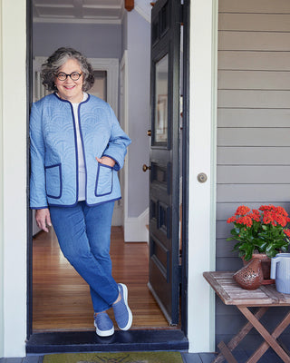 Woman in a blue outfit standing in a doorway with a plant on a table to her right. This jacket is the Fairfax Quilted Jacket sewing pattern from "Sewing the Curve" by Jenny Rushmore.