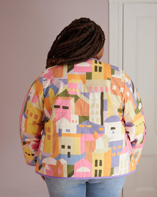 Person wearing a colorful geometric-patterned jacket indoors. This jacket is the Fairfax Quilted Jacket sewing pattern from "Sewing the Curve" by Jenny Rushmore.