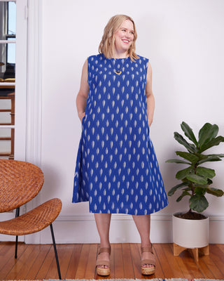 Woman wearing a blue dress with white patterns in a room with a plant and wooden furniture. This dress is the Montvale Dress & Tunic sewing pattern from "Sewing the Curve" by Jenny Rushmore.