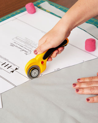 Person using a rotary cutter on craft material with a cutting mat underneath