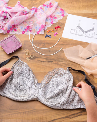 Lace bra on a wooden table with sewing materials and a design sketch.