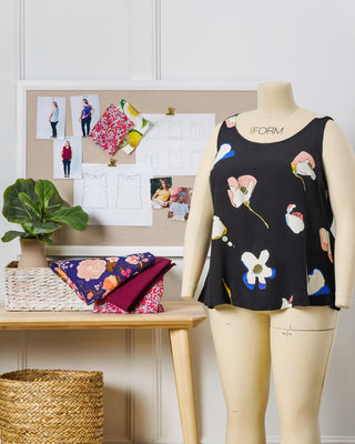 Mannequin wearing a black floral sleeveless top with beige pants in a room setting.