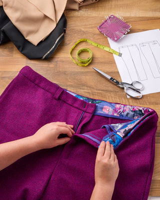 Purple fabric with floral lining on a wooden table with sewing tools.