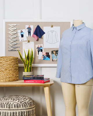 Mannequin wearing a blue shirt next to a desk with a bulletin board and books.
