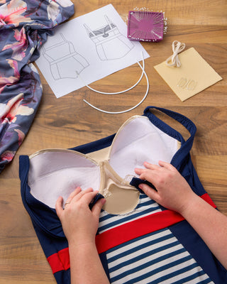 Person assembling a swimsuit with sewing materials on a wooden table. This swimsuit is the Ipswich Swimsuit sewing pattern from Cashmerette.
