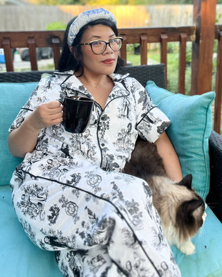 Person in pajamas holding a mug with a cat on a teal couch outdoors.