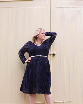 Woman wearing a navy blue dress with long sleeves against a beige wall.