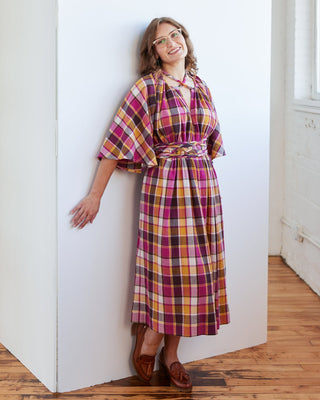 Woman wearing a plaid dress standing against a white wall. The topper is the Caroll Shrug sewing pattern from Cashmerette.