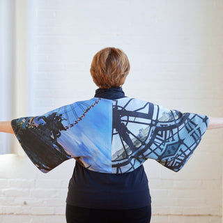 Person wearing a blue and black patterned shrug with a white background. The topper is the Caroll Shrug sewing pattern from Cashmerette.
