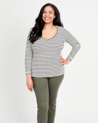 A woman standing, wearing a striped long-sleeved t-shirt and green pants. This t-shirt is the Concord T-Shirt sewing pattern from Cashmerette.