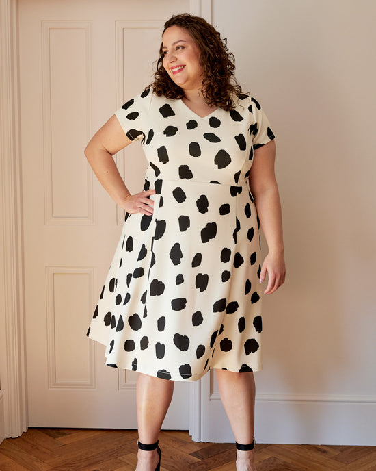 Woman wearing a polka dot dress standing against a neutral wall. This dress is the Foxhill Dress sewing pattern from "Ahead of the Curve" by Jenny Rushmore.