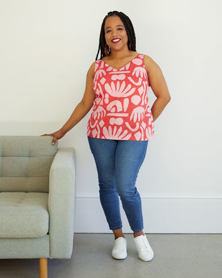 Woman wearing a red patterned top and blue jeans standing next to a gray couch. This top is the Kersoe Top sewing pattern from "Ahead of the Curve" by Jenny Rushmore.