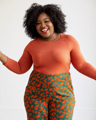 Woman wearing an orange long-sleeve top and green leggings with red leopard print on a white background. This top is the Stanway Raglan T-Shirt sewing pattern from "Ahead of the Curve" by Jenny Rushmore.