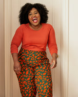 Woman wearing an orange long-sleeve top and green leggings with red leopard print on a white background. This top is the Stanway Raglan T-Shirt sewing pattern from "Ahead of the Curve" by Jenny Rushmore.