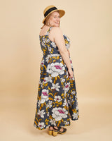 Woman wearing a floral dress and straw hat on a beige background. This is the Holyoke Maxi Dress & Skirt sewing pattern from Cashmerette.