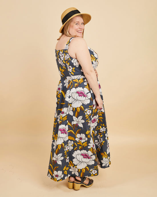 Woman wearing a floral dress and straw hat on a beige background. This is the Holyoke Maxi Dress & Skirt sewing pattern from Cashmerette.