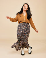 Woman wearing a mustard yellow cardigan and floral skirt on a beige background. This is the Holyoke Maxi Dress & Skirt sewing pattern from Cashmerette.