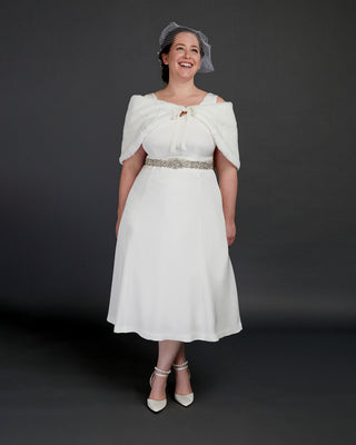 Woman wearing a white dress with a fur shrug and hat against a dark background. This dress is the Upton Dress & Skirt sewing pattern from Cashmerette.