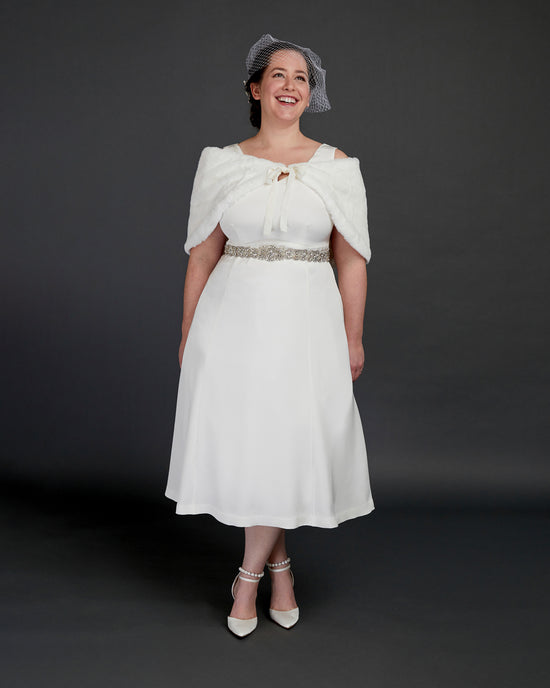 Woman wearing a white dress with a fur shrug and hat against a dark background. This dress is the Upton Dress & Skirt sewing pattern from Cashmerette.