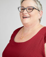 Woman wearing glasses and a red top with a gold necklace on a white background. This dress is the Upton Dress & Skirt sewing pattern from Cashmerette.