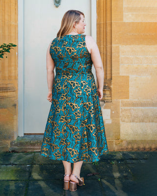 Woman wearing a blue and gold patterned dress standing in front of a stone building.. This dress is the Upton Dress & Skirt sewing pattern from Cashmerette.